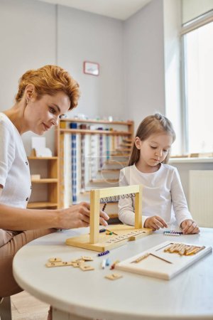 Montessori-Konzept, Mädchen spielen pädagogisches Spiel in der Nähe des Lehrers, Kleiderbügel für Farbperlentreppen