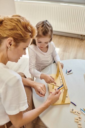 Montessori-Konzept, Mädchen zeigt auf Kleiderbügel für Farbperlentreppen in der Nähe einer Lehrerin, von oben gesehen