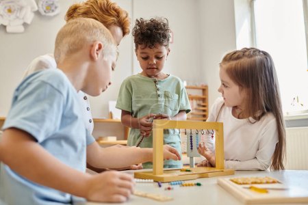 Téléchargez les photos : Mignons enfants regardant un garçon afro-américain jouer à un jeu éducatif à l'école montessori, la diversité - en image libre de droit