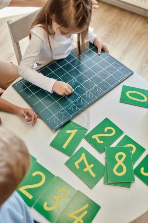 Foto de Vista superior de niña escribiendo números en pizarra, aprendiendo a contar en la escuela Montessori - Imagen libre de derechos