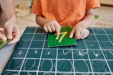 smart girl counting near teacher, chalkboard, learning how to count in Montessori school, cropped