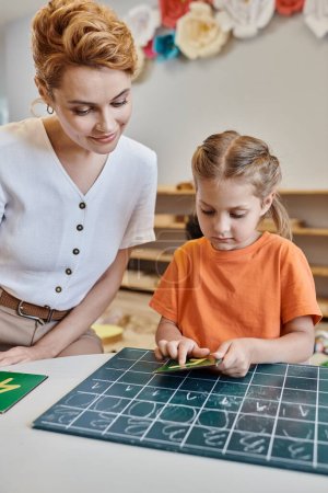 Kluges Mädchen zeigt auf Zahl neben Lehrer, zählt Tafel, lernt spielerisch, Montessori