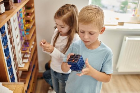 neugieriger Junge mit Montessori-Perlenmaterial, lernt Mathe, Mädchen auf verschwommenem Hintergrund