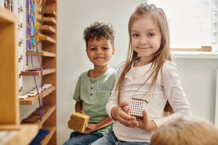 cheerful girl holding cube with beads near african american boy, diversity, Montessori school