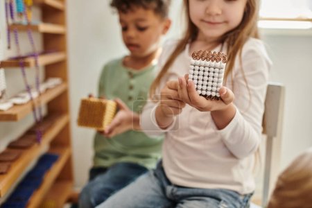 smiling girl holding cube with beads near african american boy, diversity, Montessori school