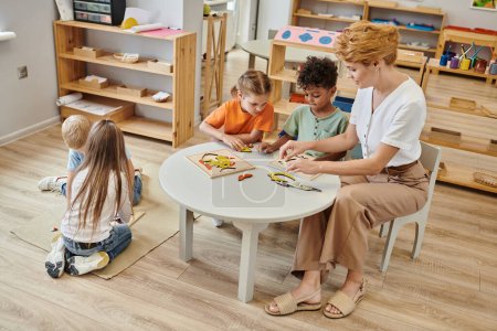 female teacher using didactic montessori material while playing with interracial kids, diversity
