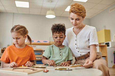 teacher using didactic montessori material while playing with interracial boy and girl, diverse