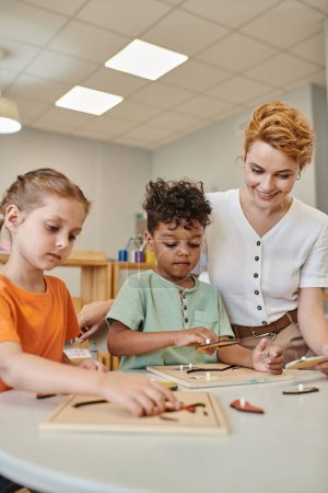 maestra usando material didáctico montessori mientras juega con niños interracial en la escuela