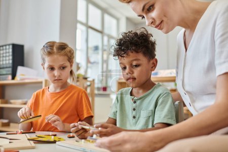 interrassische Kinder spielen mit didaktischem Montessori-Material in der Nähe von Lehrerinnen, Vielfalt