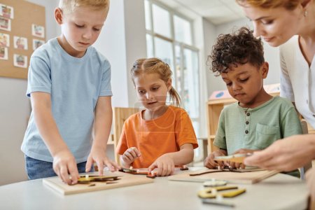 interrassische Kinder spielen mit didaktischem Montessori-Material in der Nähe des Lehrers in der Schule, lernen und spielen