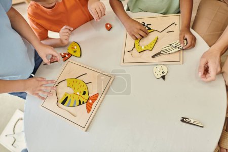 von oben, beschnittene interrassische Kinder, die in der Schule mit didaktischem Montessori-Material spielen, Puzzle
