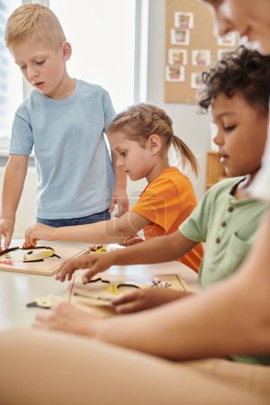 niños multiétnicos y el profesor utilizando materiales didácticos durante la lección en la escuela montessori
