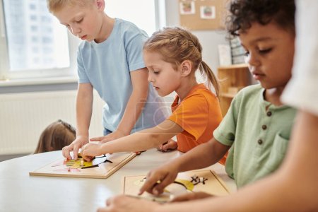 Téléchargez les photos : Enfants interraciaux jouant avec du matériel didactique sur la table à l'école montessori - en image libre de droit
