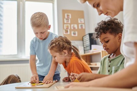 Lehrer und multiethnische Kinder spielen mit didaktischen Materialien in der Montessori-Schule