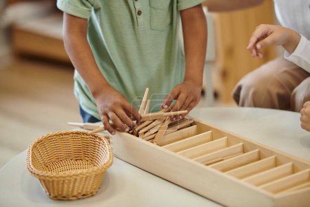 cropped view of african american boy holding wooden sticks near girl in montessori school