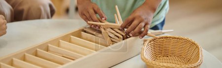 partial view of african american boy holding wooden sticks during lesson in montessori class, banner