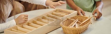 cropped view of interracial children playing with wooden sticks in montessori school, banner