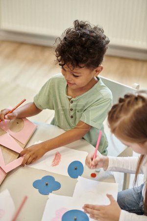Blick auf lächelnde multiethnische Kinder beim Zeichnen während des Unterrichts in der Montessori-Schule