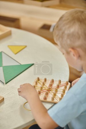 boy playing with rubber bands and wooden sticks during lesson in montessori school