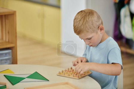 boy playing with rubber bands and wooden board on table during lesson in montessori school