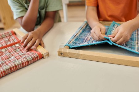 cropped view of multiethnic kids playing with cloth and buttons during lesson in montessori school
