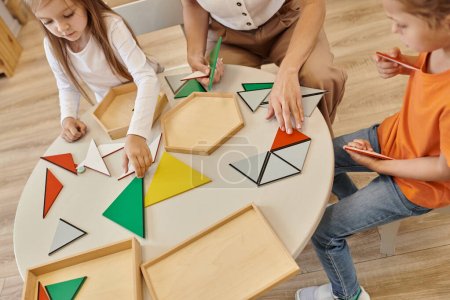 Foto de Vista de ángulo alto del profesor y los niños jugando con triángulos en la mesa en la escuela montessori - Imagen libre de derechos