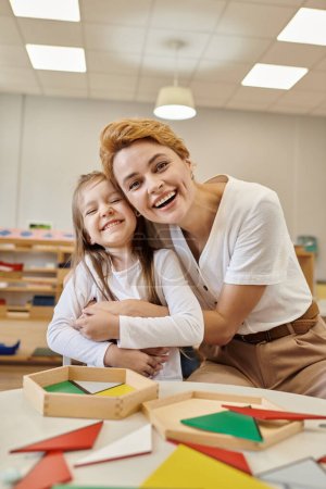 Photo for Positive teacher hugging pupil near didactic material in montessori school - Royalty Free Image