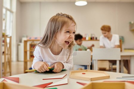 Photo for Cheerful kid looking away near didactic materials in class of montessori school - Royalty Free Image