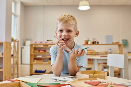 fröhlicher Junge mit Dreiecken beim Spiel im Klassenzimmer der Montessori-Schule