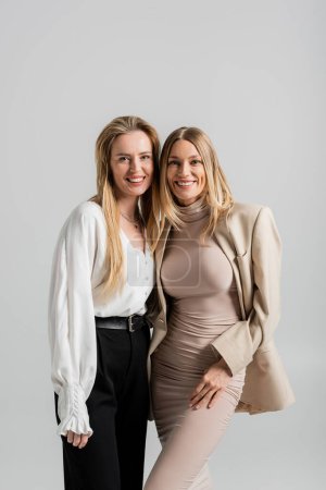 zwei hübsche blonde Schwestern in formeller Kleidung lächelnd und einander umarmend, Modekonzept