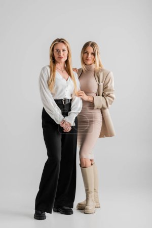 atractivas hermanas con estilo en traje formal posando sobre fondo gris, vinculación, concepto de moda