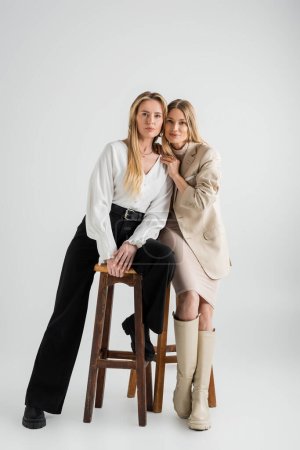 two fashionable stylish sisters in formal outfits sitting on chairs, fashion and style concept