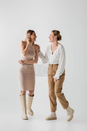 zwei trendige, stylische blonde Schwestern in pastellfarbenen Outfits, die einander anlächeln, Stil und Mode
