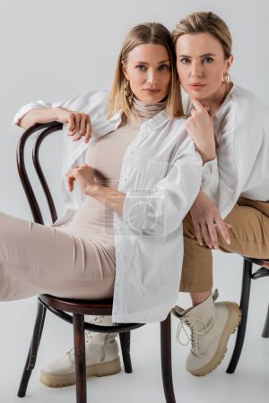 elegantes hermanas rubias elegantes sentadas en sillas con atuendo pastel de moda, concepto de moda