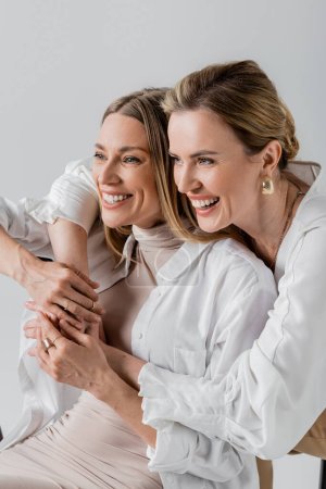 Foto de Dos hermanas voguish alegre en ropa formal abrazos sonriendo y mirando hacia otro lado, el estilo y la moda - Imagen libre de derechos