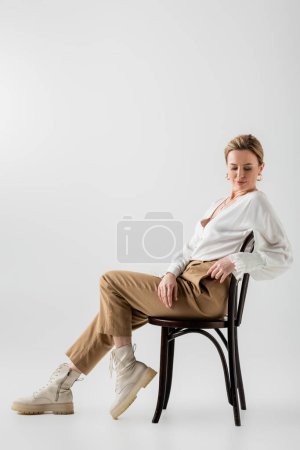 stylish blonde woman in stylish formal attire sitting on chair and relaxing, style and fashion