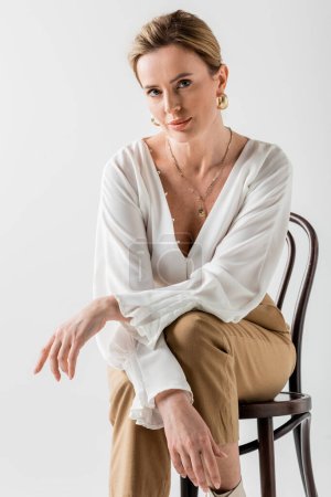 Téléchargez les photos : Femme blonde élégante assise sur une chaise et relaxante avec ses bras croisés, style et mode - en image libre de droit
