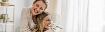 pretty sisters in trendy attire hugging and smiling sincerely on kitchen backdrop, bonding, banner