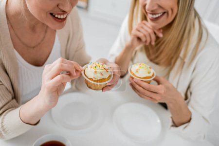 Foto de Vista recortada de hermanas guapas en degustación de ropa de moda y disfrutar de cupcakes, vinculación familiar - Imagen libre de derechos