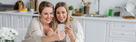 Téléchargez les photos : Deux sœurs blondes en belle tenue faisant selfie sur fond de cuisine, liens familiaux, bannière - en image libre de droit