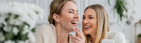 Photo for Two blonde sisters in lovely attire laughing and holding mobile phone, family bonding, banner - Royalty Free Image