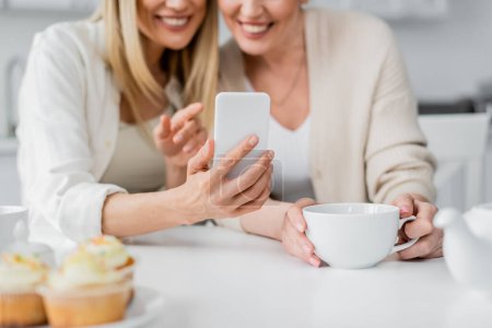 cropped view of pretty classy sisters making selfie and smiling on kitchen background, bonding