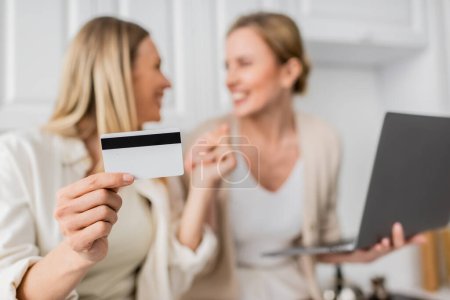 close up two pretty trendy sisters in pastel outfit holding credit card, blurred, family bonding