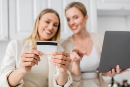 Foto de Primer plano bien parecido hermanas de moda en la cocina con el ordenador portátil que sostiene la tarjeta de crédito, borrosa, vinculación - Imagen libre de derechos