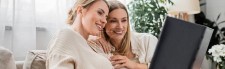 Photo for Young blonde sisters hugging and looking at photo album on white curtain backdrop, bonding, banner - Royalty Free Image