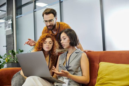 bearded team lead near businesswomen working on laptop in office, planning startup, teamwork