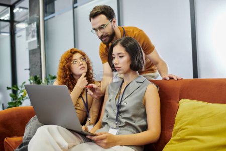 Bärtiger Teamleiter zeigt auf Laptop in der Nähe junger Frauen, die Startup-Projekt in Coworking-Büro planen