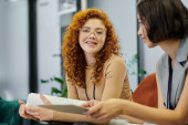 optimistic redhead manager in eyeglasses discussing business project with colleague in modern office Poster #673222478