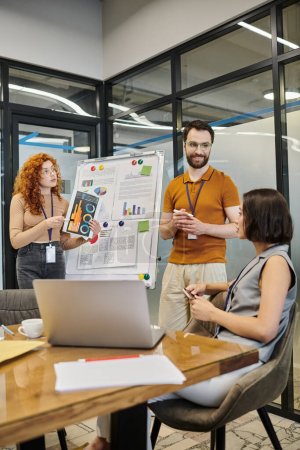 redhead manager with infographics near bearded colleague and businesswoman in meeting room