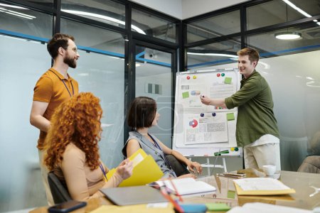 Geschäftsprojekt planen, lächelnder Unternehmer zeigt auf Grafiken in der Nähe von Kollegen im Besprechungsraum